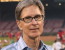 fenway sports group owner john henry wearing a plaid blue shirt and glasses standing in front of a sports pitch