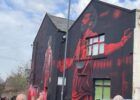 a mural of mo salah with his arms outstretched on the side of a house close to anfield