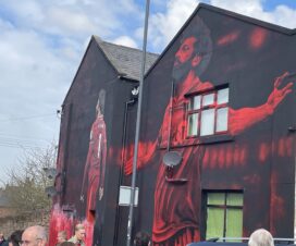 a mural of mo salah with his arms outstretched on the side of a house close to anfield