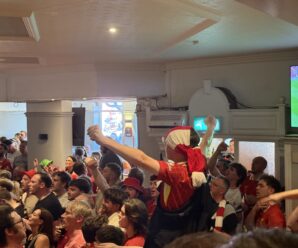 a young lad with a scarf around his head has his arms aloft whilst others below him celebrate liverpool's title win