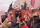 virgil van dijk wearing sunglasses and holding the premier league trophy on the back of the bus during the parade as countless people take his photograph with mobile phones