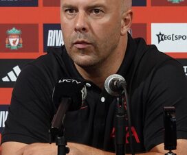 arne slot in a black liverpool training top in front of some microphones