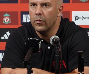 arne slot in a black liverpool training top in front of some microphones